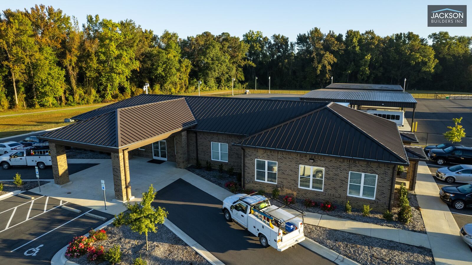 A low drone view of a brick commercial building with a covered drop-off and a service truck out front