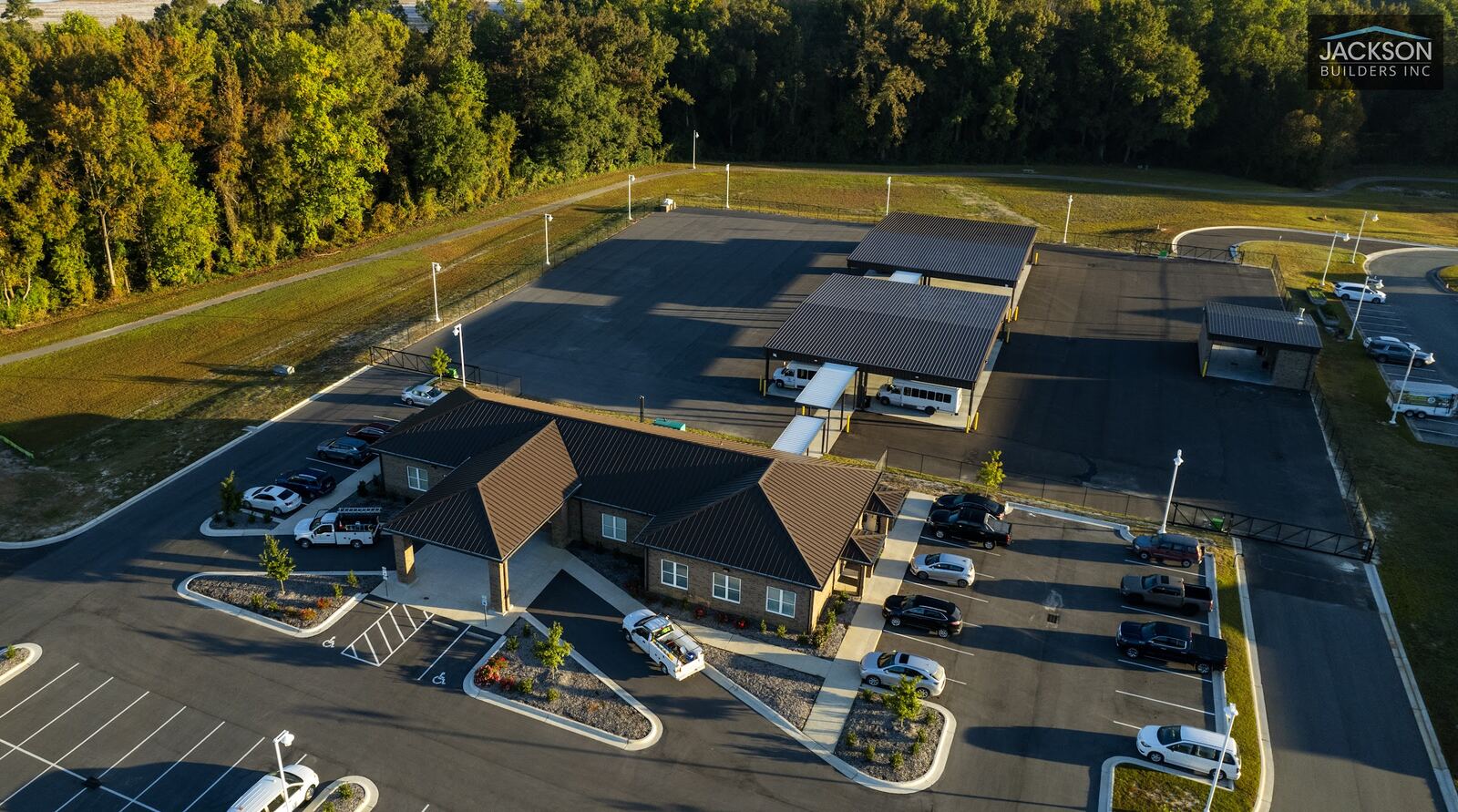 A drone view over a new commercial campus, with parking lots and covered structures against a tree line