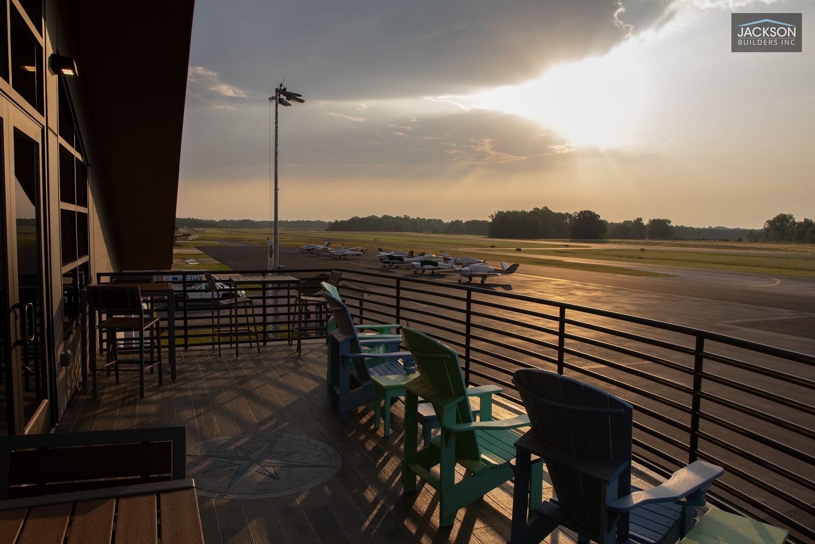 Sun breaking through clouds over the runway, seen from the terminal's upper balcony with lounge chairs along the rail