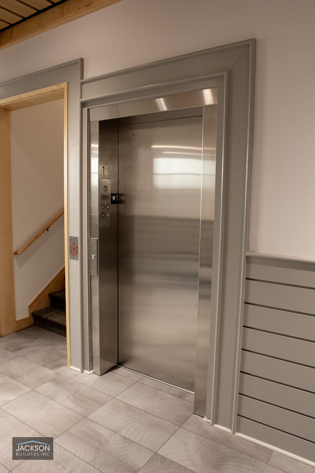 A brushed steel elevator door set into a pale wood-trimmed hallway