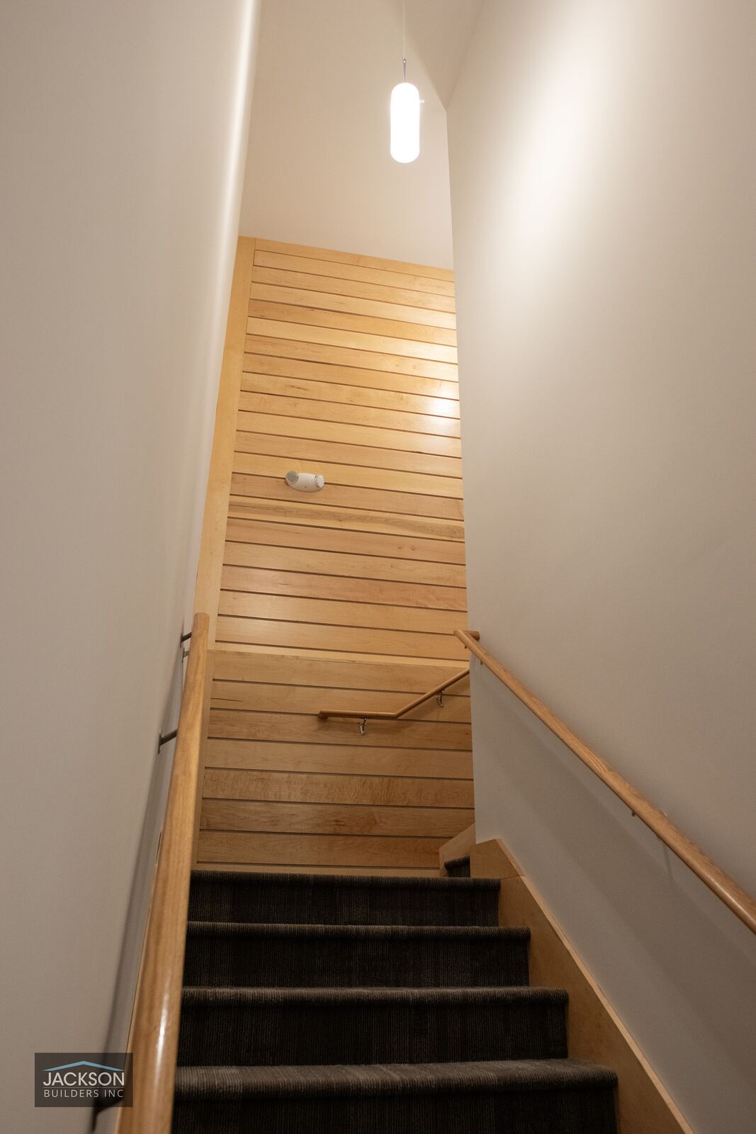A narrow stairwell with warm wood treads and a single arched window at the top
