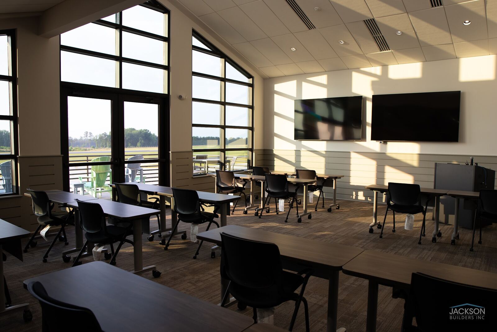An upstairs conference and lounge room with tall windows, wall-mounted screens, and tables set in rows